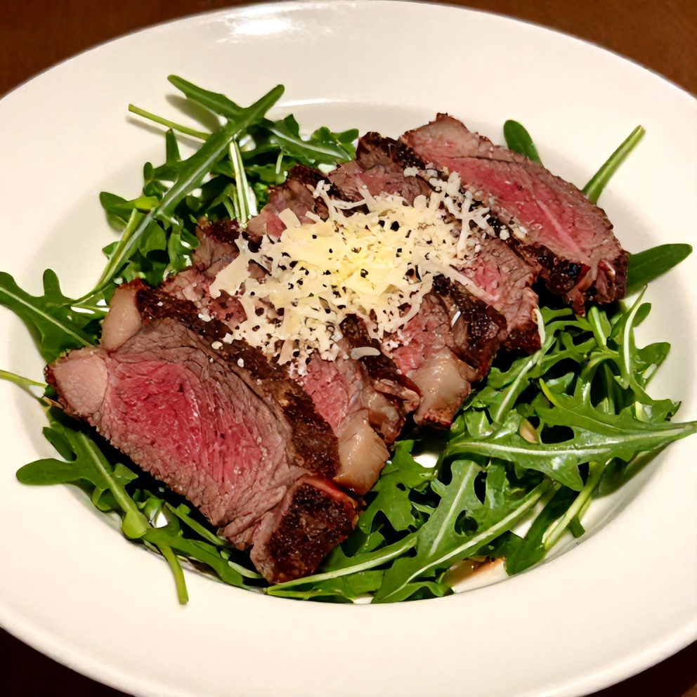 Plated steak and arugula salad garnished with shaved Parmesan and cracked black pepper in a white bowl